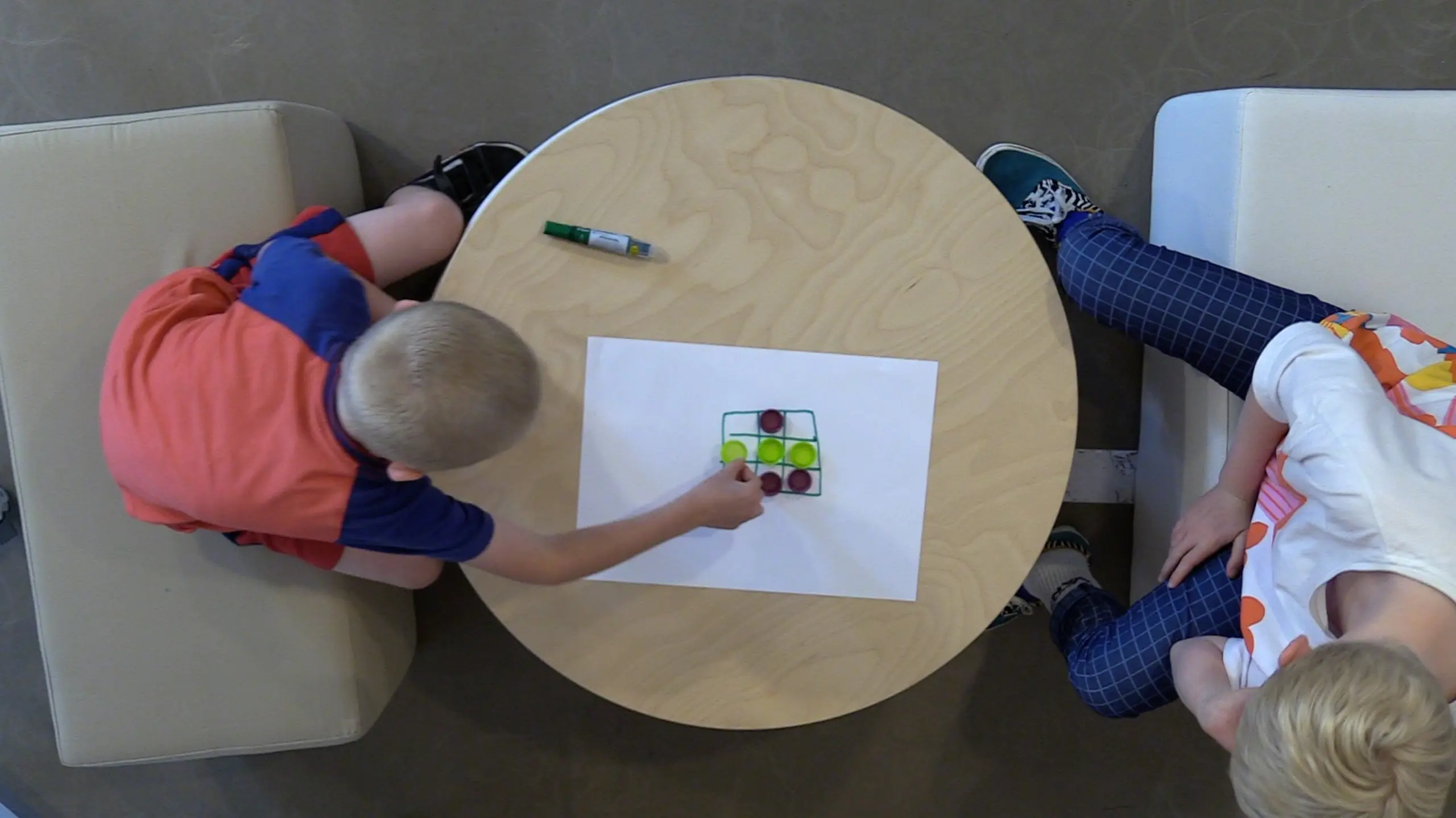 children playing Tic Tac Toe with bottle caps and a piece of paper